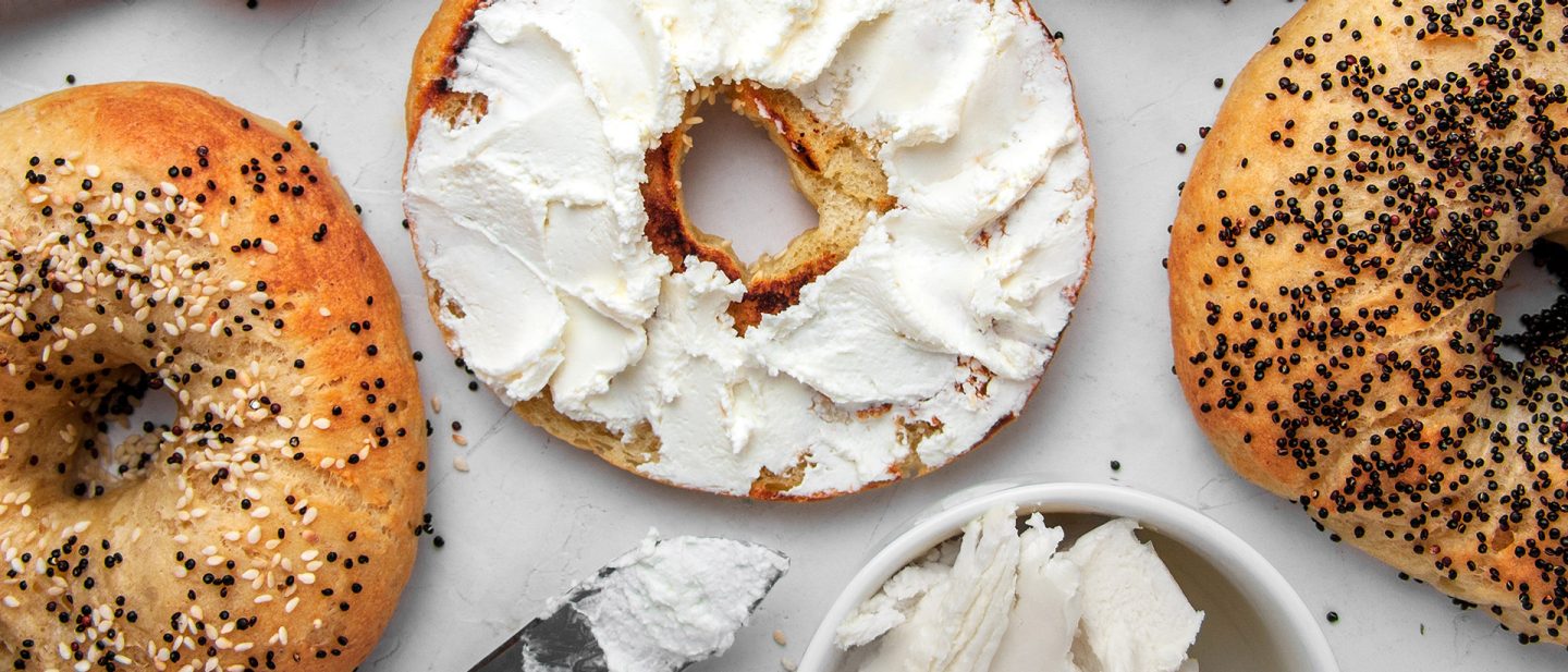 Photo of fresh bagels with cream cheese and sesame seeds, top view on surface.