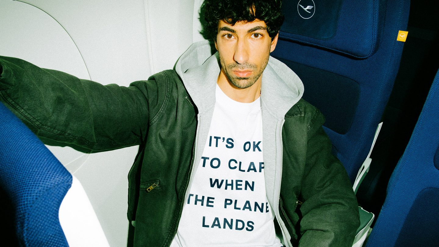 Person sitting in an airplane seat wearing a T-shirt with the text 'It’s ok to clap when the plane lands.'