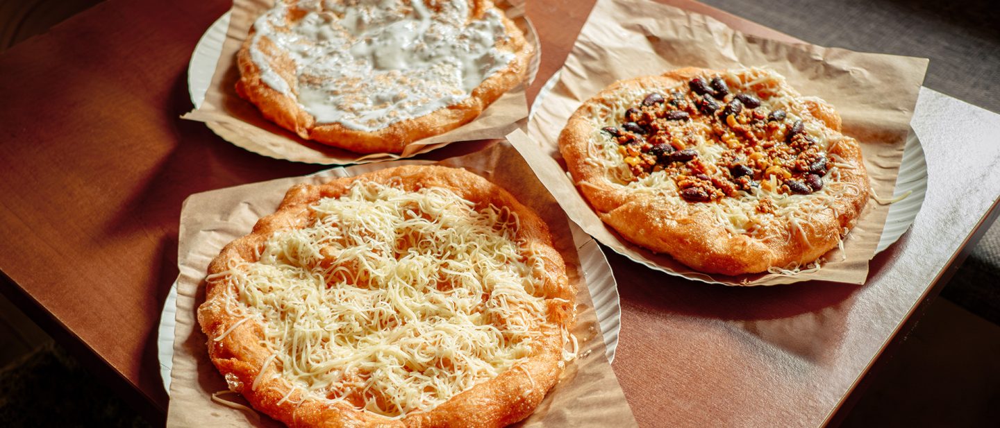 Foto von drei verschiedenen Arten von frisch gebackenem Lángos mit Käse und verschiedenen Belägen auf einem Holztisch