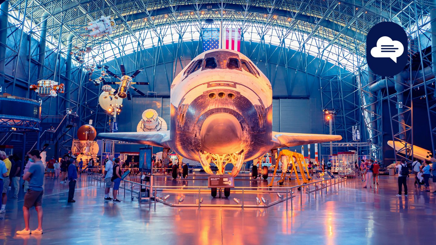 Foto eines Spaceshuttles, das in einem Museum in Washington, D. C., ausgestellt ist, umgeben von Besucher:innen und Weltraumausstellungsstücken