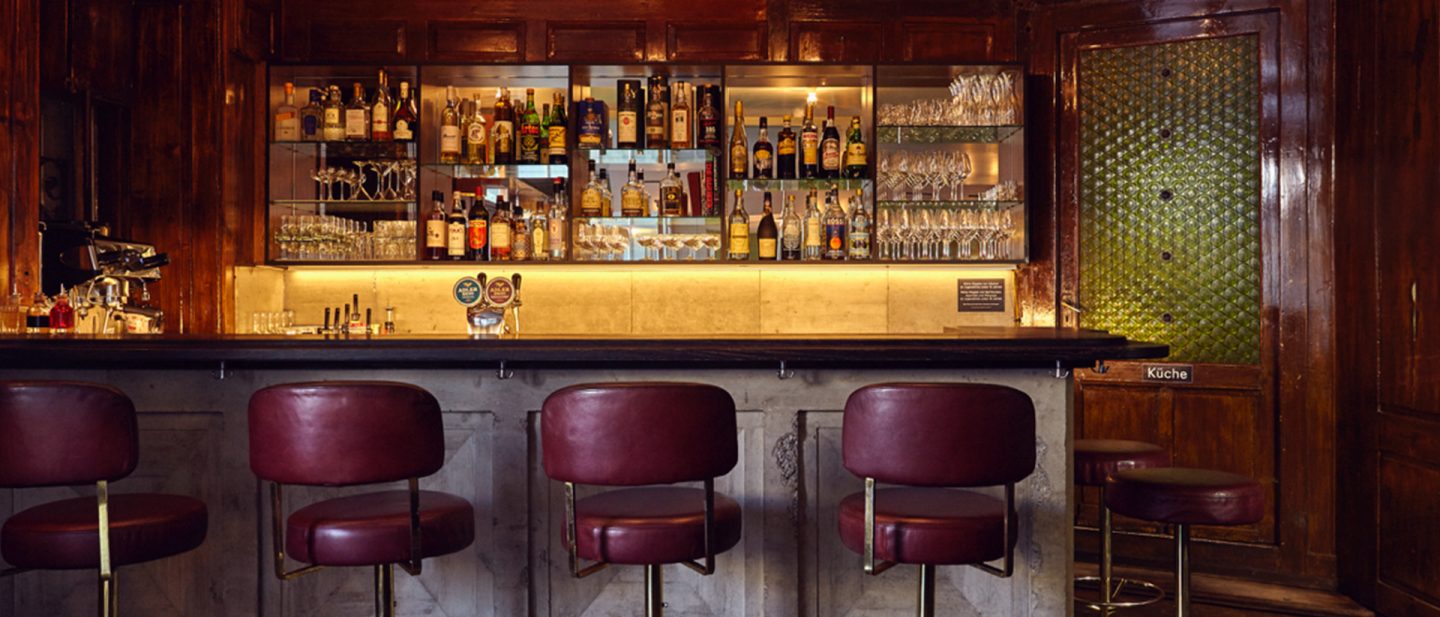 Bar interior of the Schnupf restaurant with wooden stools and a well-stocked shelf of drinks.