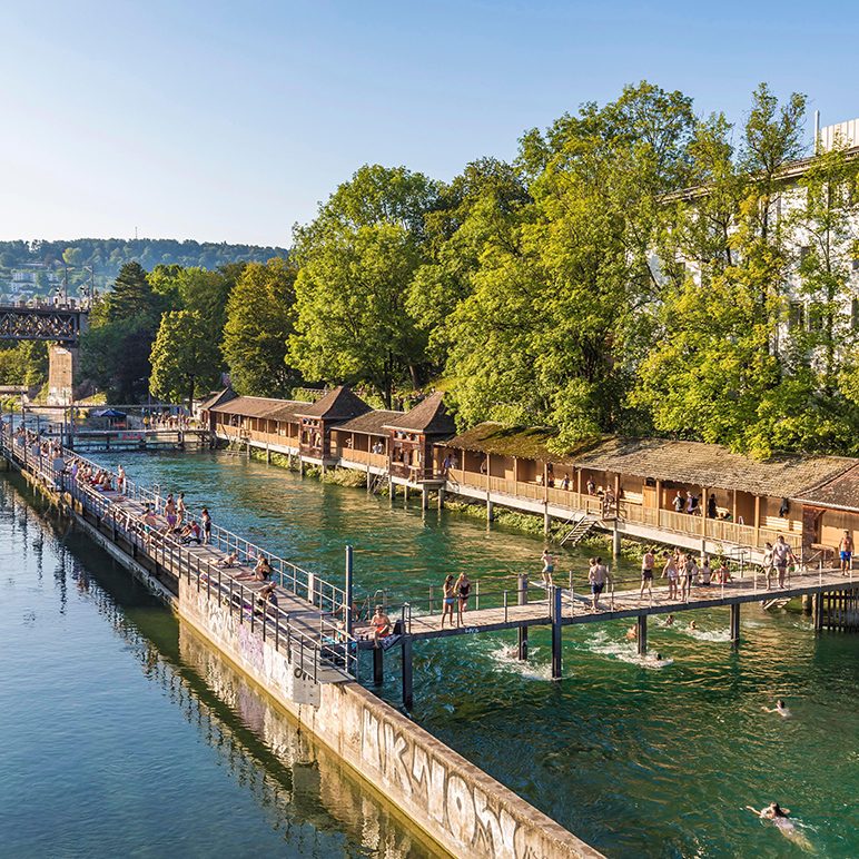 Scenic view of the Unterer Letten river pool including lush trees, with people enjoying a summer's day.