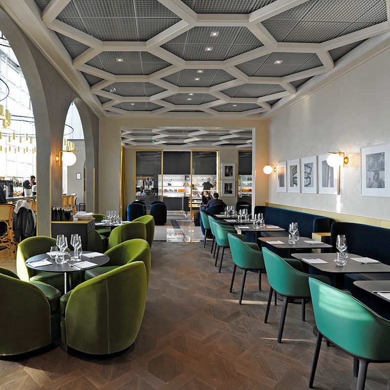 Modern restaurant with green velvet chairs, a honeycomb ceiling, and elegant lighting