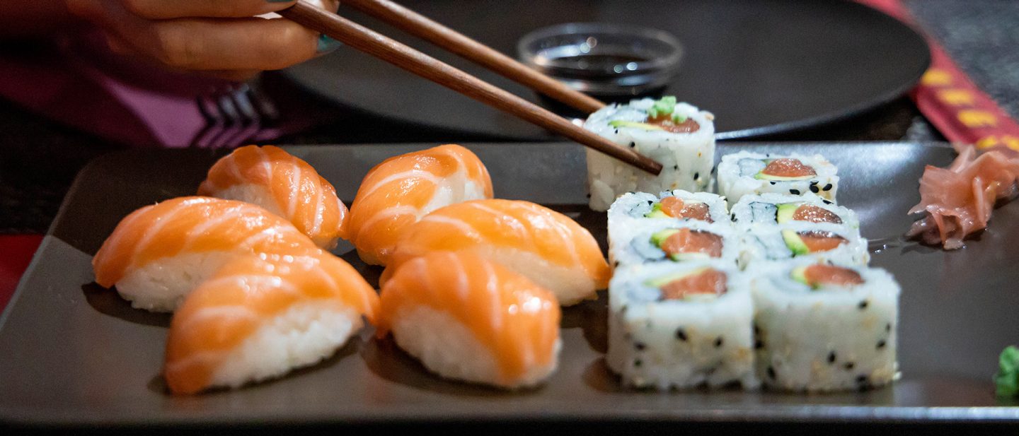 Salmon nigiri and sushi rolls on a plate, with a person using chopsticks