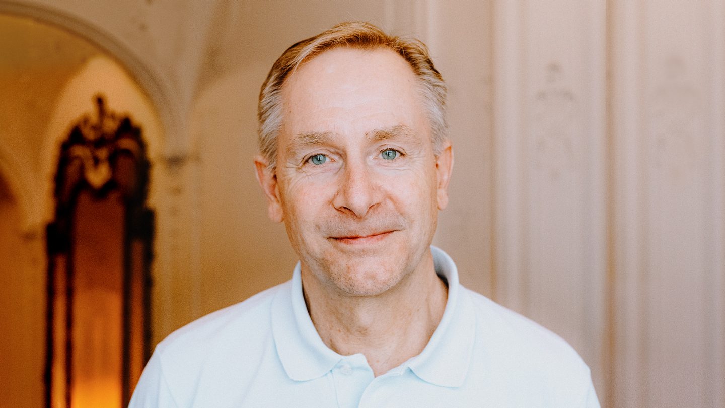 Portrait of a smiling man in front of a warmly lit architectural background.
