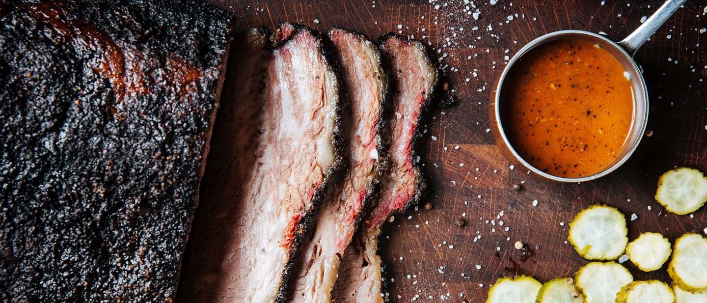 Sliced beef brisket with BBQ sauce and pickles on a wooden cutting board