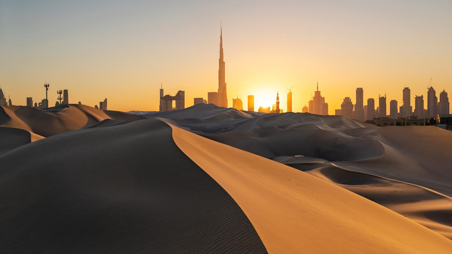 Sunset over sand dunes with the Dubai skyline and Burj Khalifa in the background
