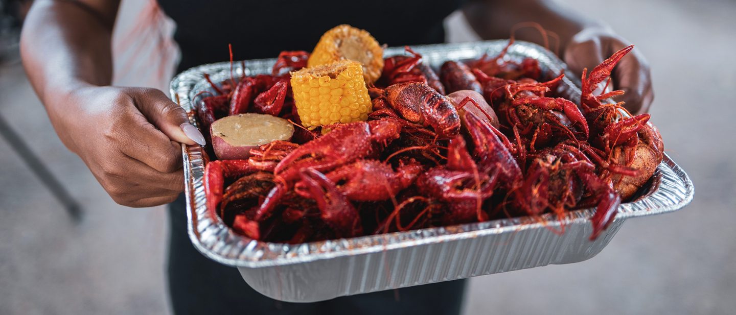 A person holds a tray of boiled crawfish, corn on the cob, and potatoes