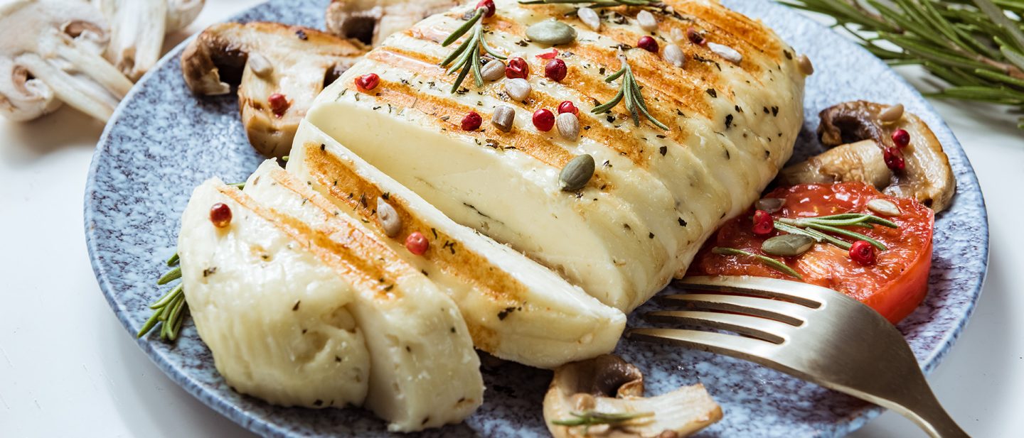Close-up of grilled halloumi cheese with sear marks, served with mushrooms, tomatoes, and fresh herbs