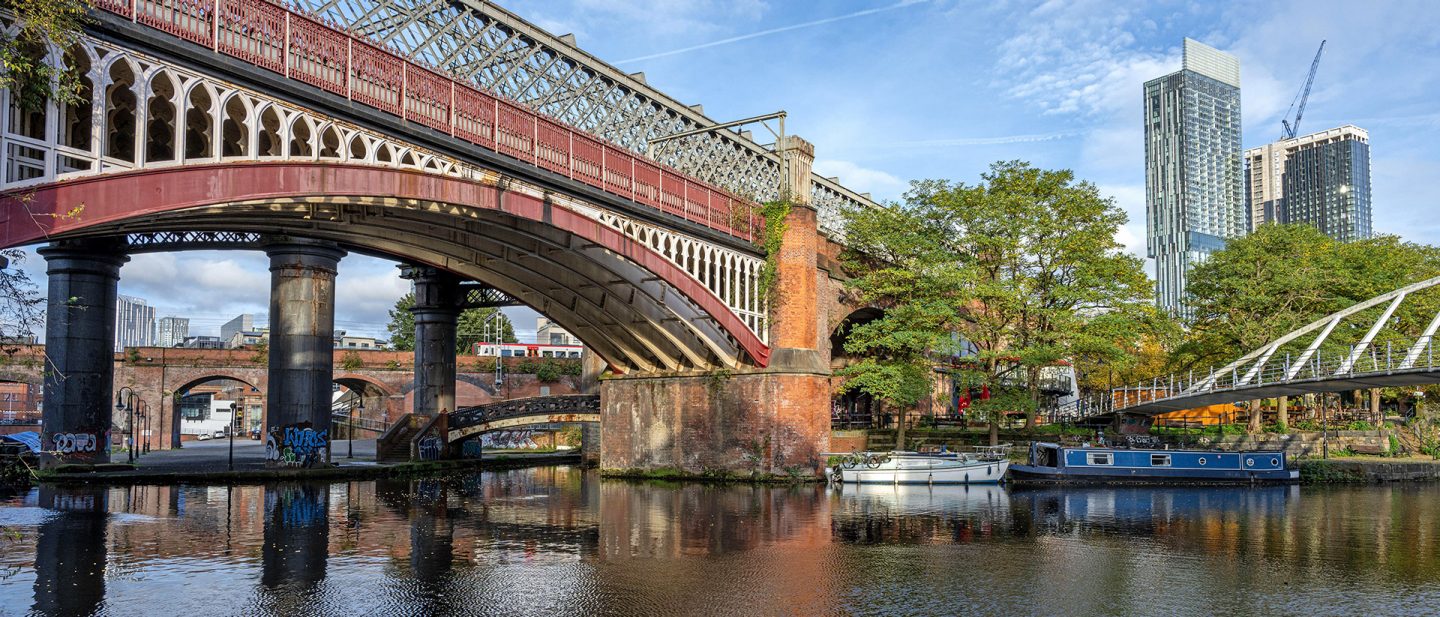 Castlefield in Manchester featuring historic railway bridges, canal boats, and modern skyscrapers