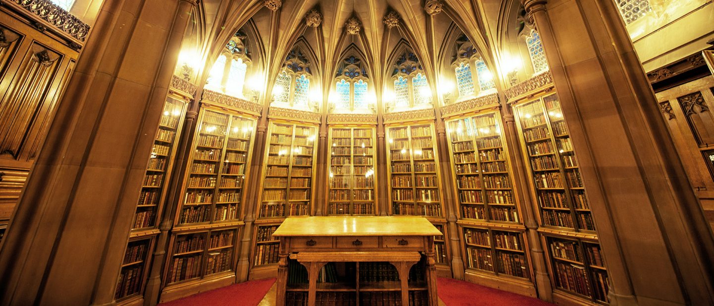 Interior view of the John Rylands Library featuring neo-Gothic architecture, tall bookshelves, and a historic reading table