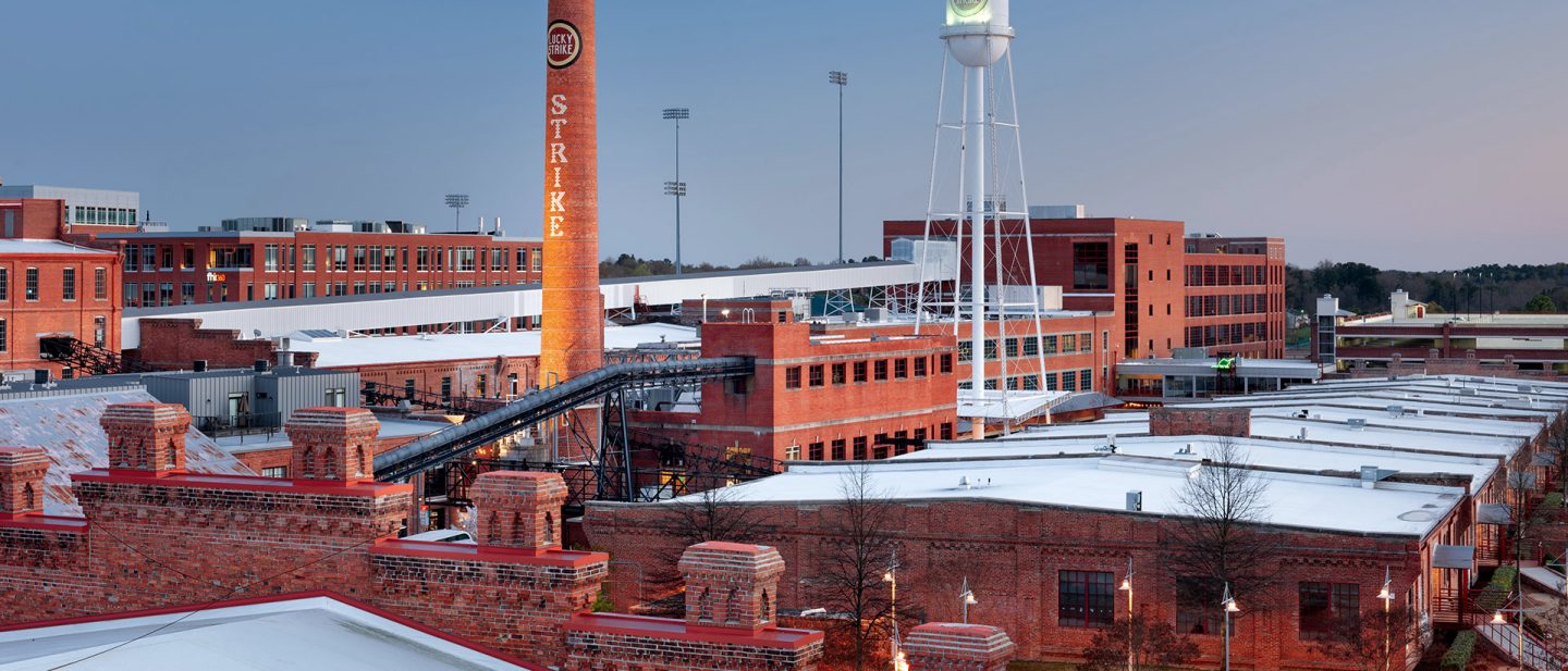 Historic brick industrial buildings with a tall chimney and water tower in a renovated factory district at dusk.