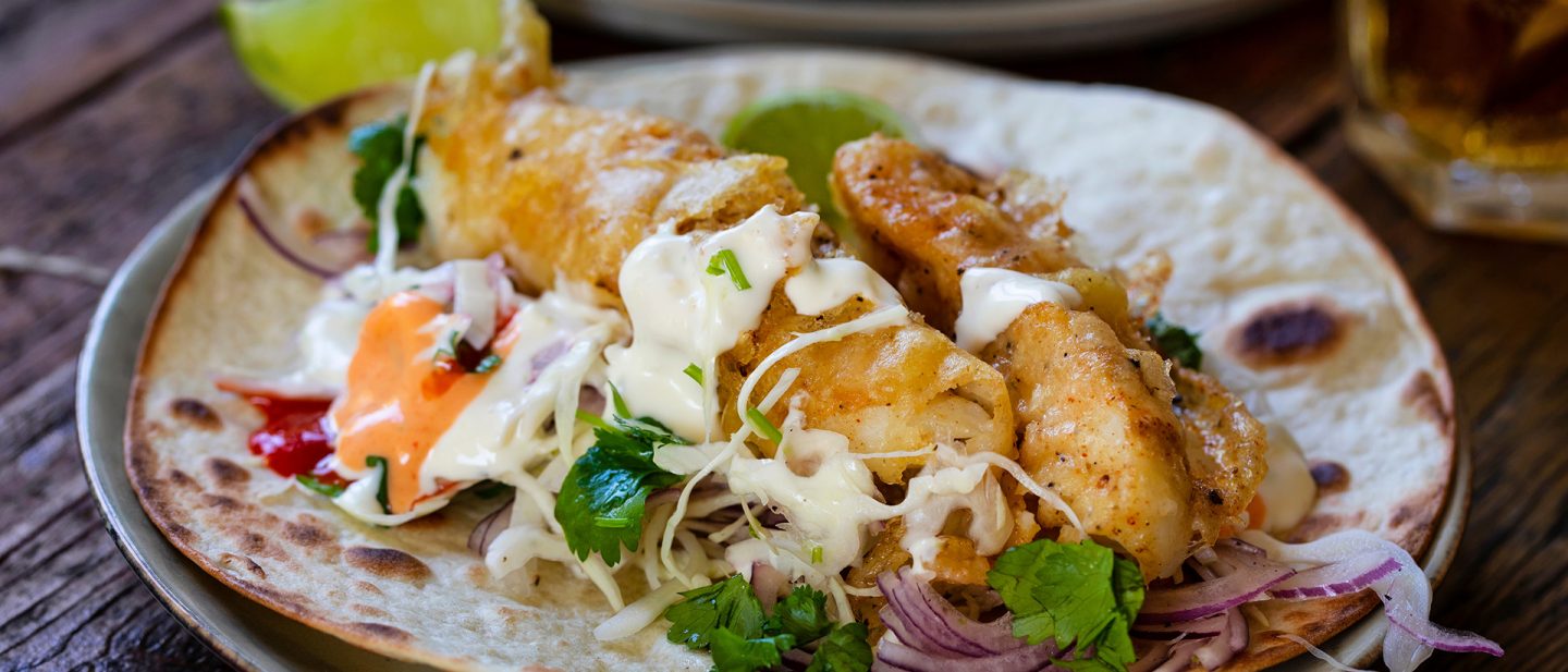 A fresh fish taco featuring crispy battered fish on a tortilla with cabbage slaw and creamy sauces