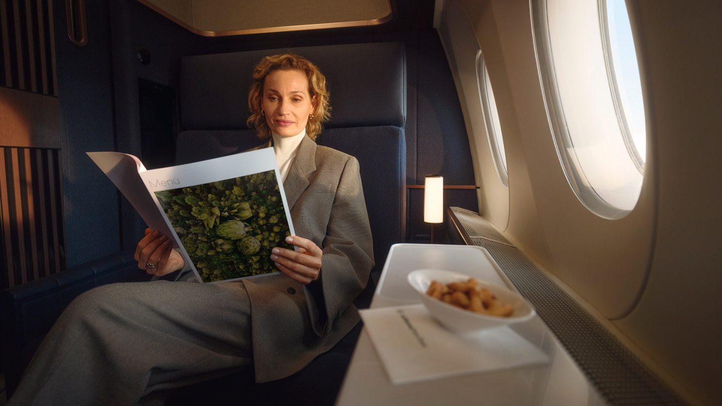Woman relaxing in a First Class airplane cabin reading a menu by the window in natural light