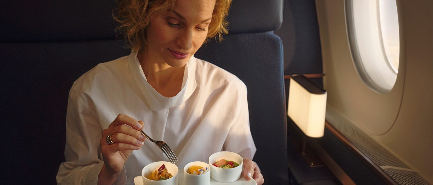 Passenger enjoying a multi-course meal in First Class with small appetizers by the airplane window