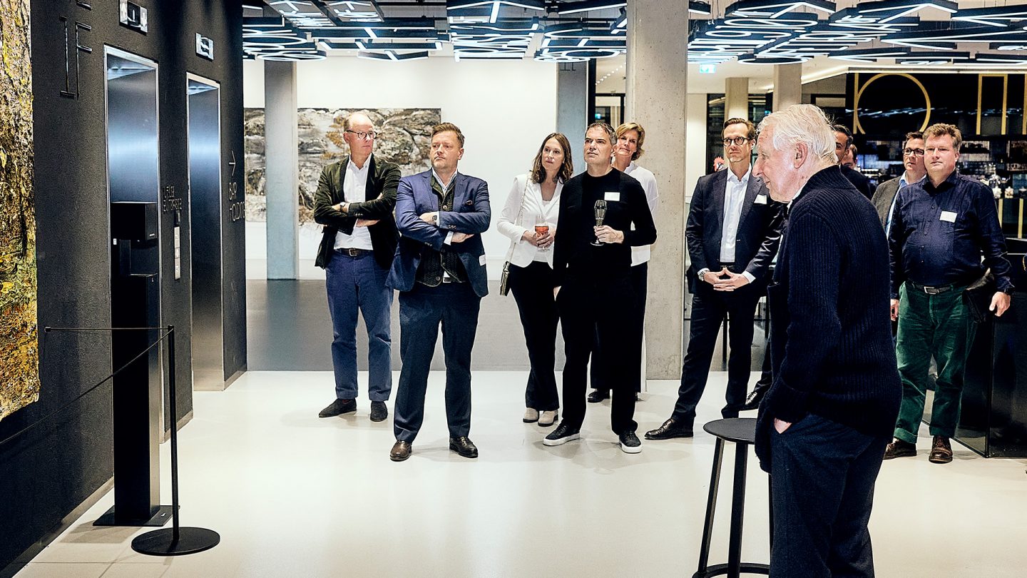 A group of people in business attire view a large art installation in a modern interior setting.