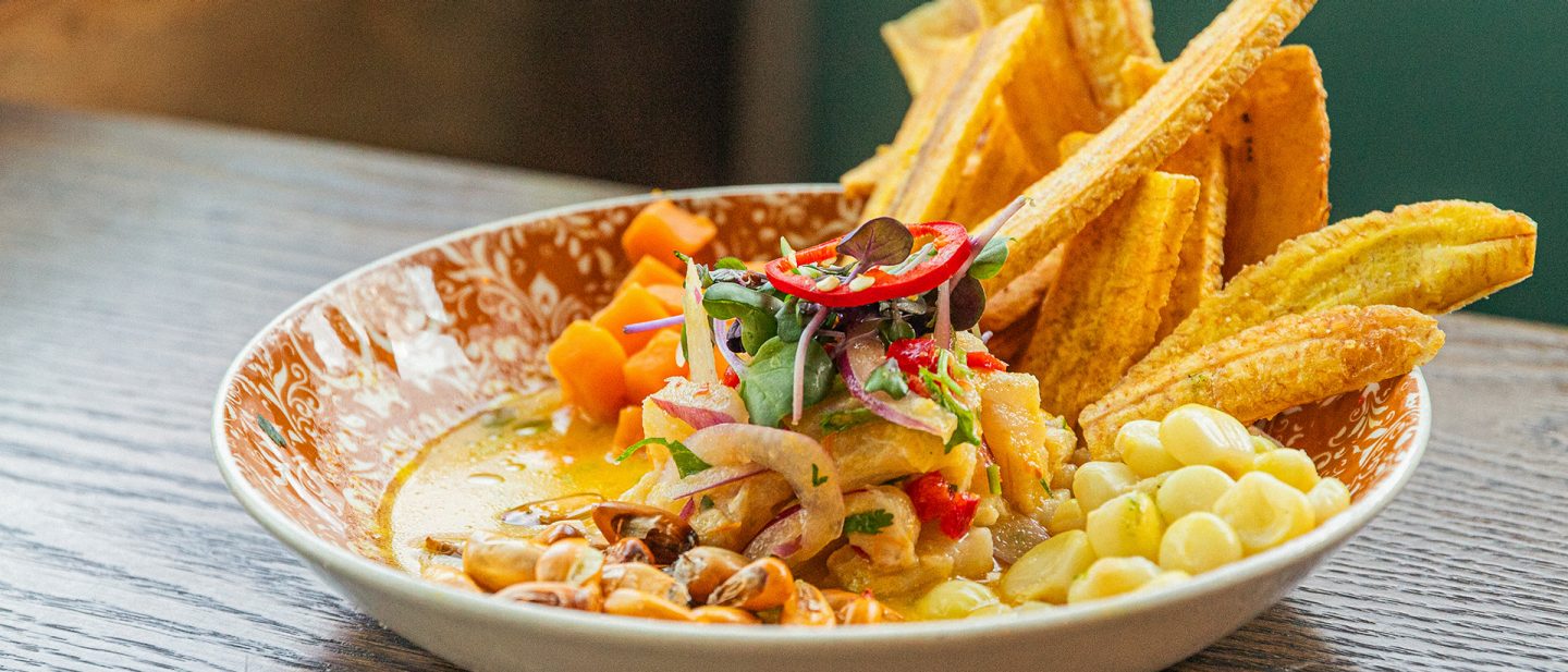 Plate with ceviche, corn, sweet potato, and crispy plantain chips on wooden table