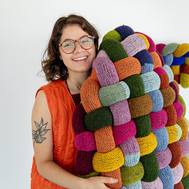 Katrina Sanchez holding colorful knitted textile art piece