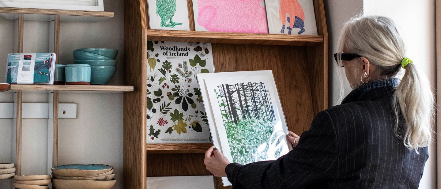Woman examining art prints in a wooden shelf display at a shop in Dublin's Creative Quarter