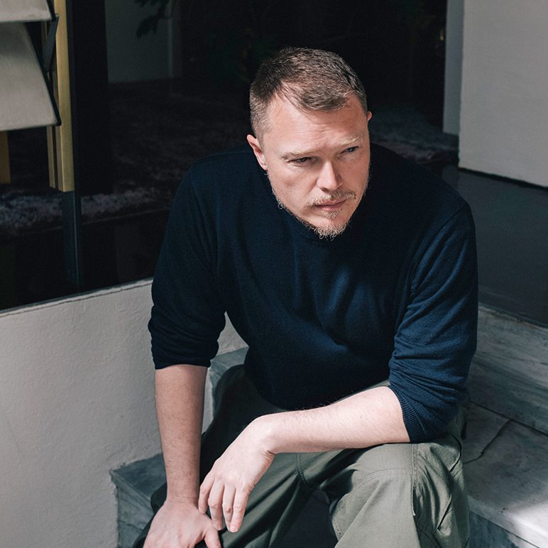Hannes Peer wearing a dark blue sweater, seated on steps