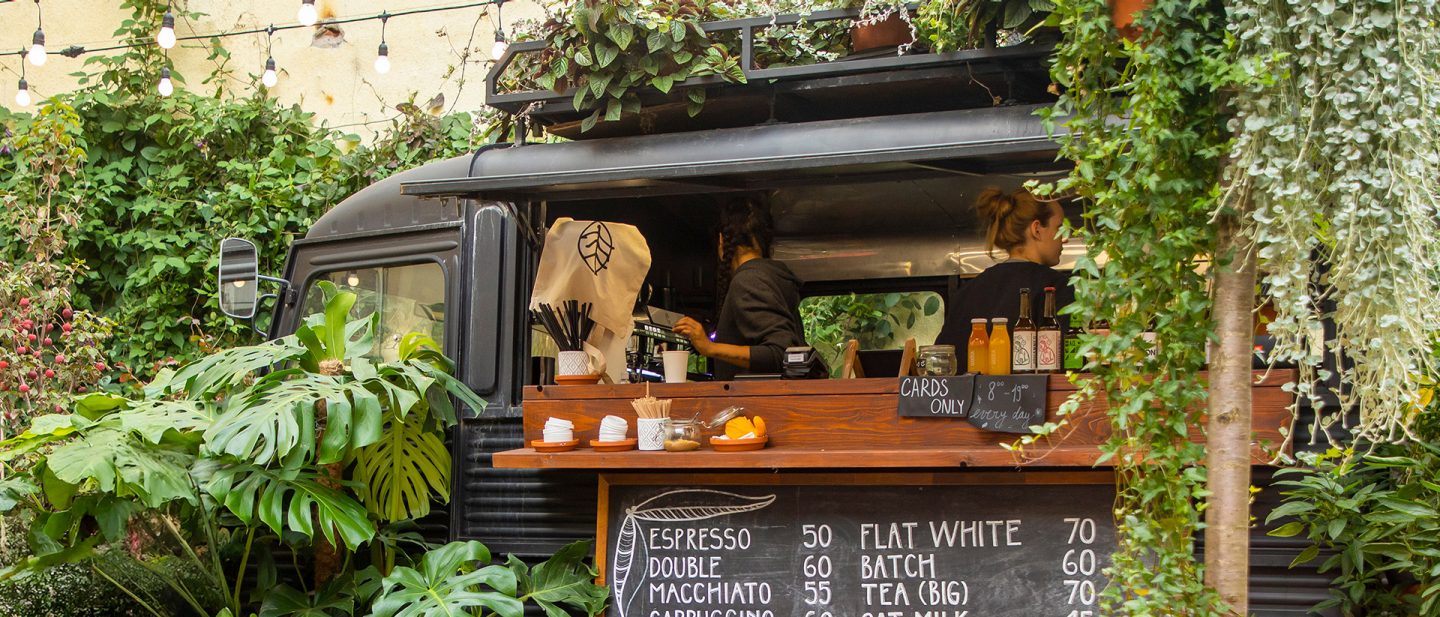 A coffee truck in a leafy courtyard with hanging lights