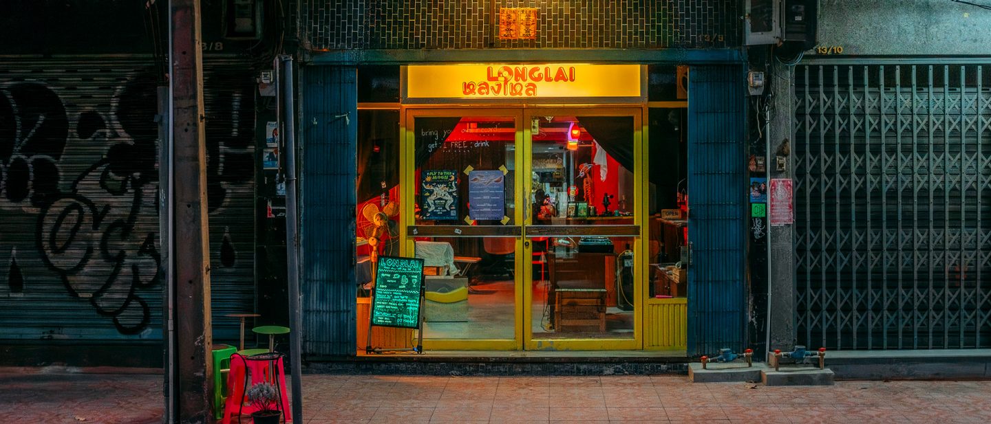 Night view of the brightly lit yellow storefront of the Longlai Bar between closed shops