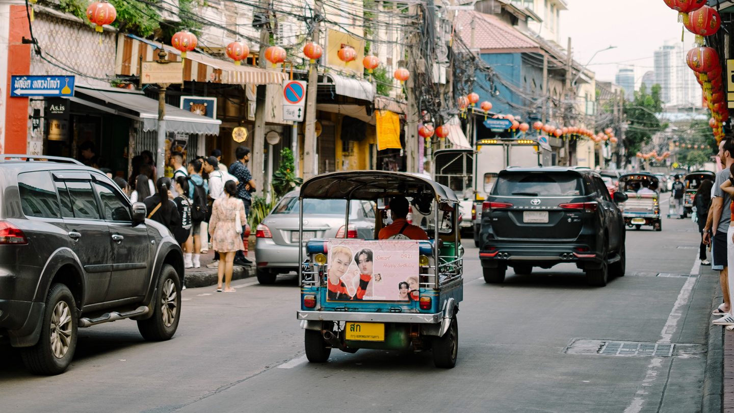 A tuk-tuk drives through Song Wat Road in Bangkok with red lanterns and heavy traffic
