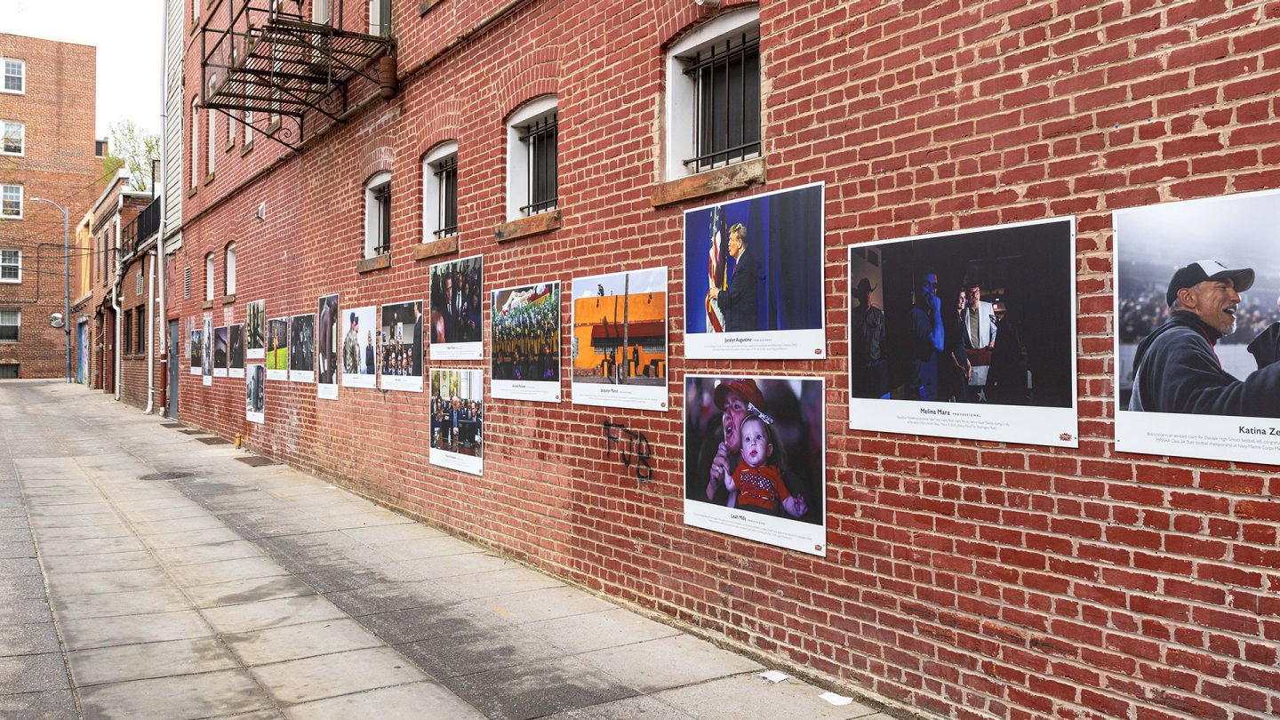 Outdoor photo exhibition on a brick wall at the Lost Origins Gallery.