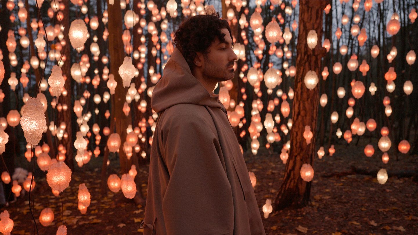 Ali Gallefoss im Profil vor einem dunklen Wald mit vielen leuchtenden, orangefarbenen Lichtern