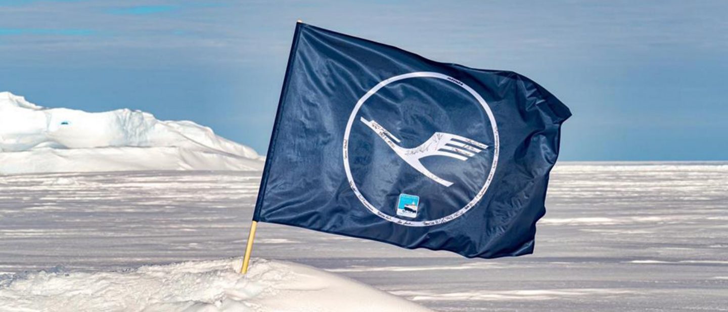 A dark blue flag with a crane logo flying in the snow against an icy landscape