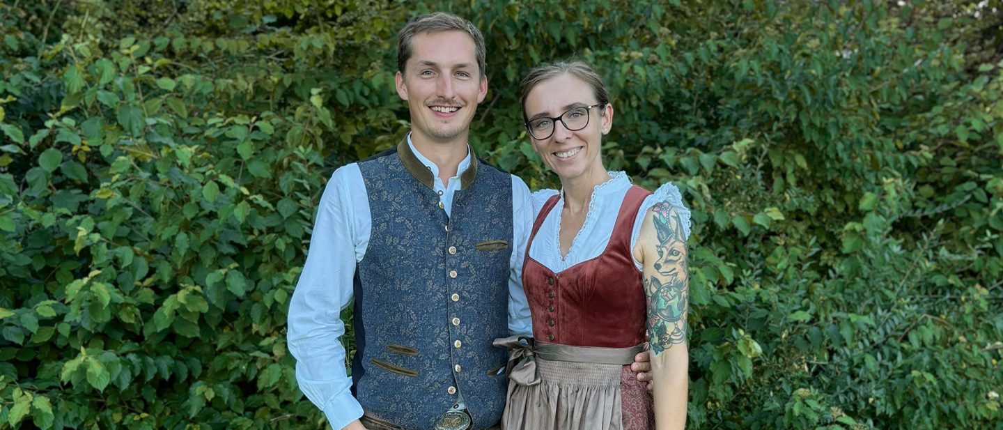 Couple in traditional clothing smiling in front of a green backdrop.