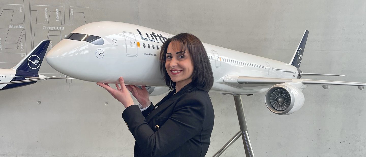 A smiling woman in a blazer holds her hands under a large model airplane