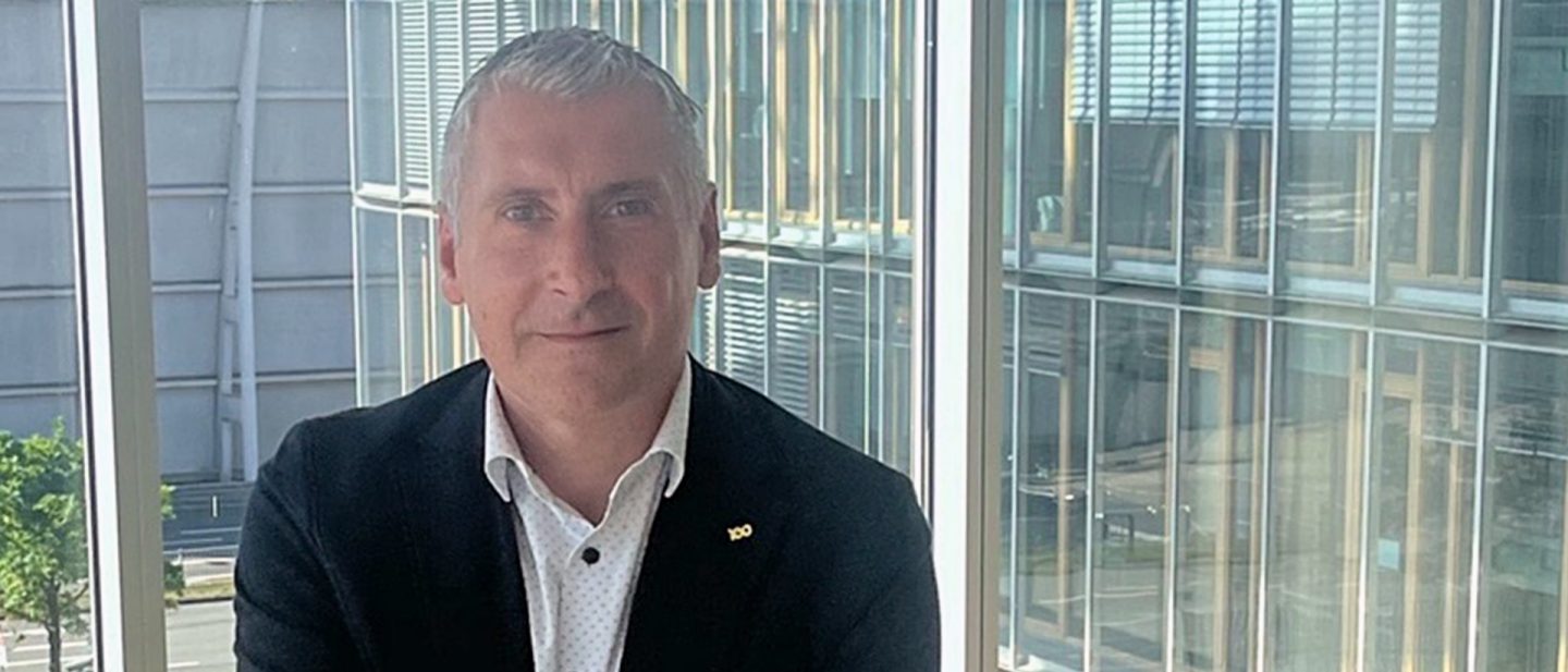 Portrait of a man in a blazer in front of a large glass façade