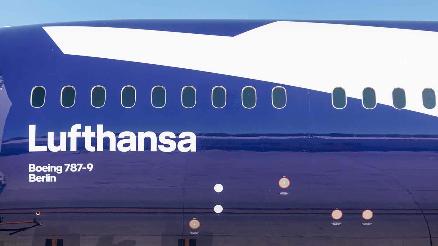 Close-up van de blauwe Lufthansa Boeing 787-9 romp, met de witte belettering en een rij ramen
