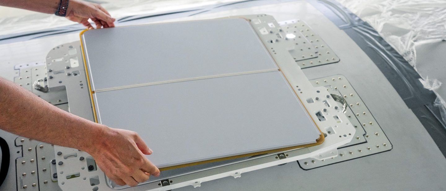 An individual covers a white box with a white sheet, blending the two objects together visually.