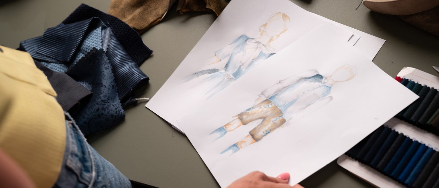 Fashion sketches of traditional clothing on a table next to fabric swatches and threads