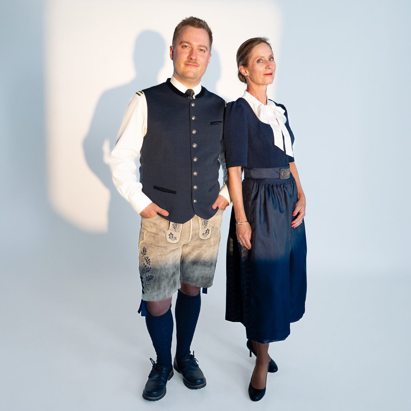 A man and woman in blue Lufthansa traditional uniforms with lederhosen and dirndl against a white backdrop