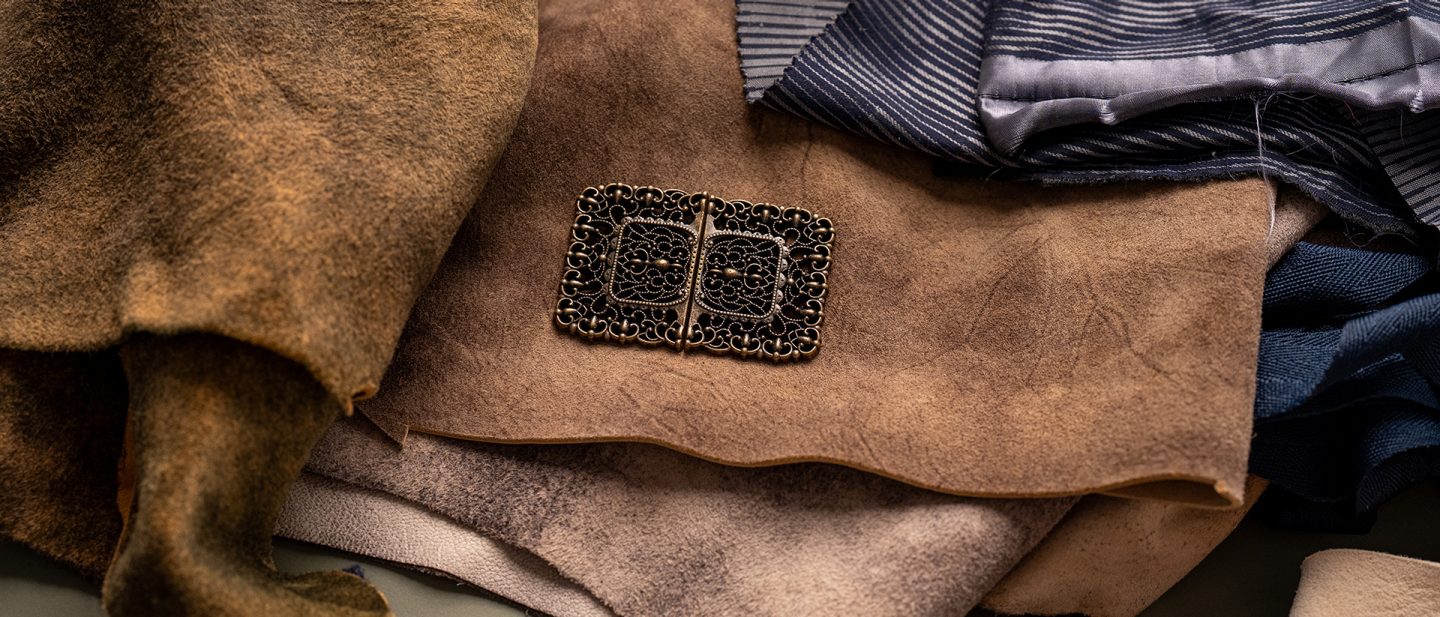 An ornate traditional belt buckle rests on brown leather pieces and blue fabric