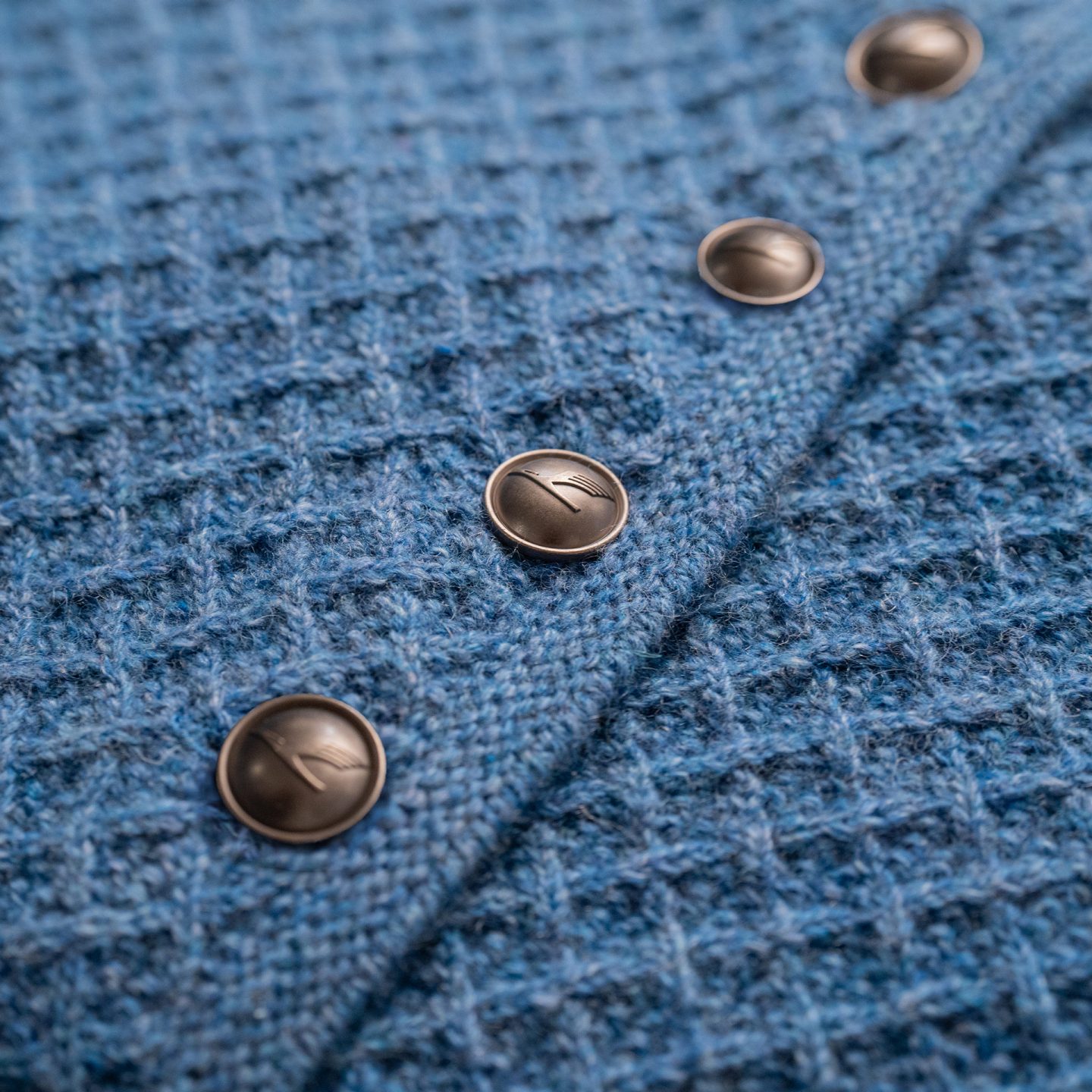 Close-up of a blue knitted vest with metal buttons featuring a crane logo