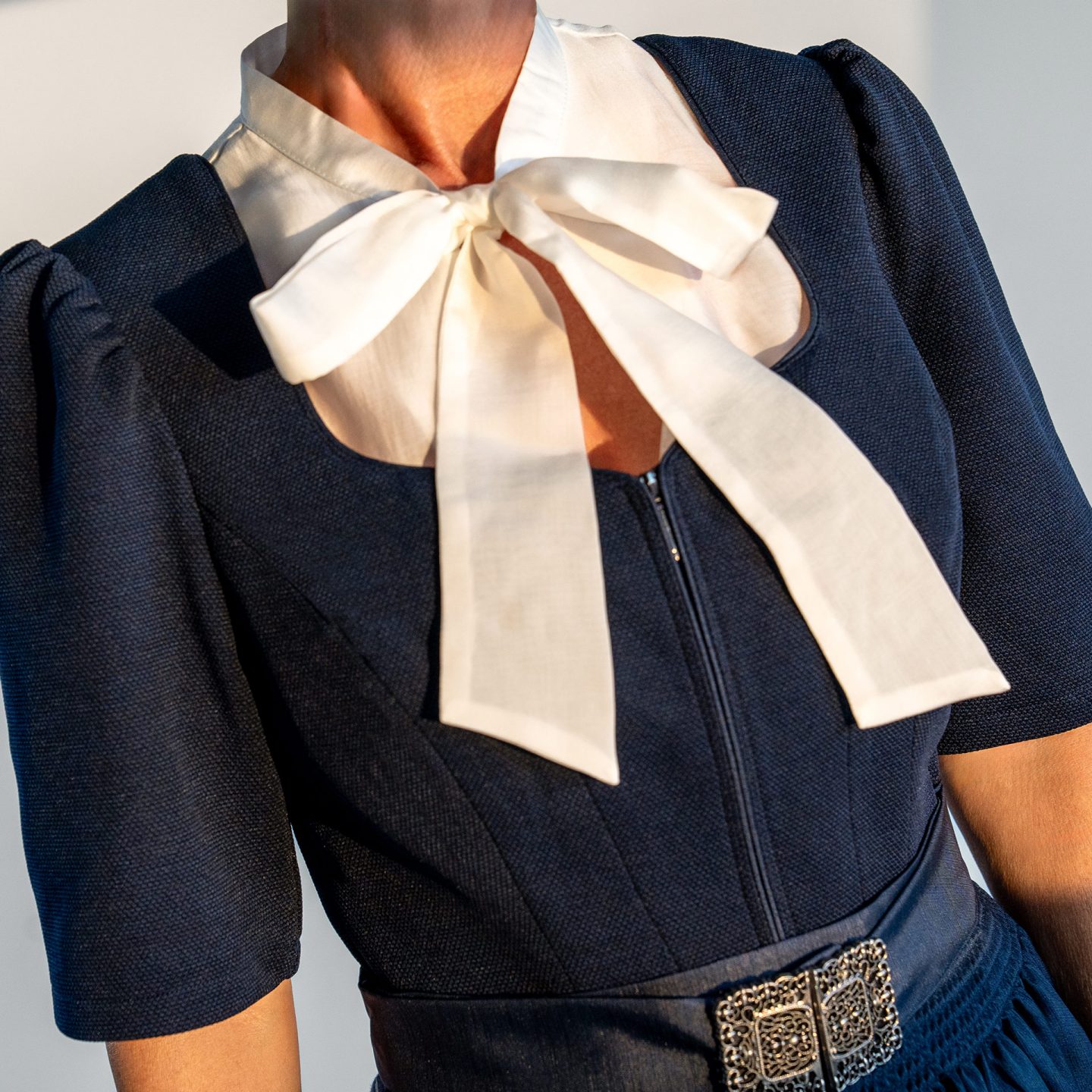 Close-up of a dark blue dirndl bodice featuring a white bow blouse and an ornate apron buckle