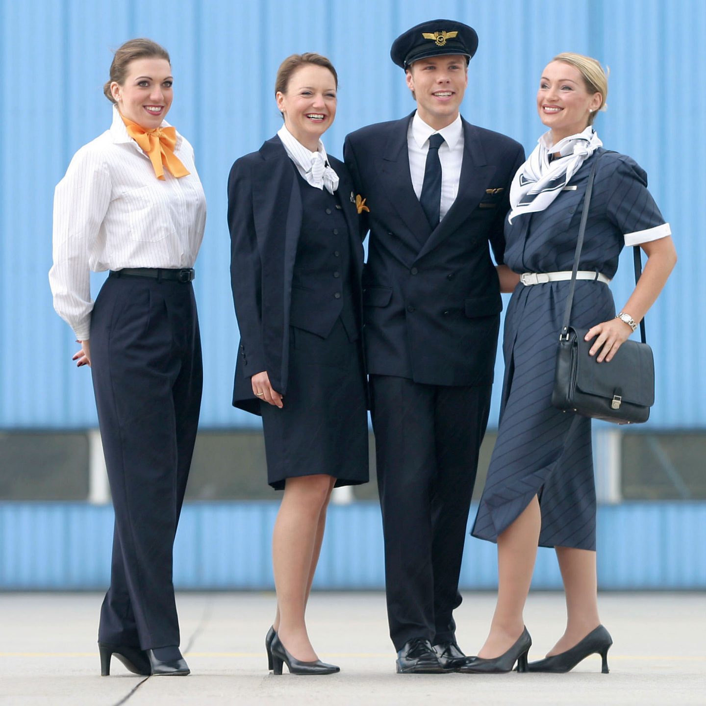 Lufthansa crew in navy uniforms; pilot with cap, attendants with blouses, scarves, and skirts.