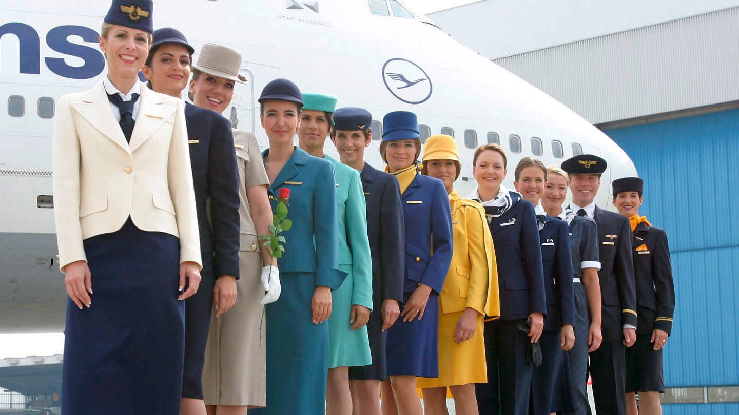 Lufthansa crew in different uniforms from the past stand in front of a large aircraft.
