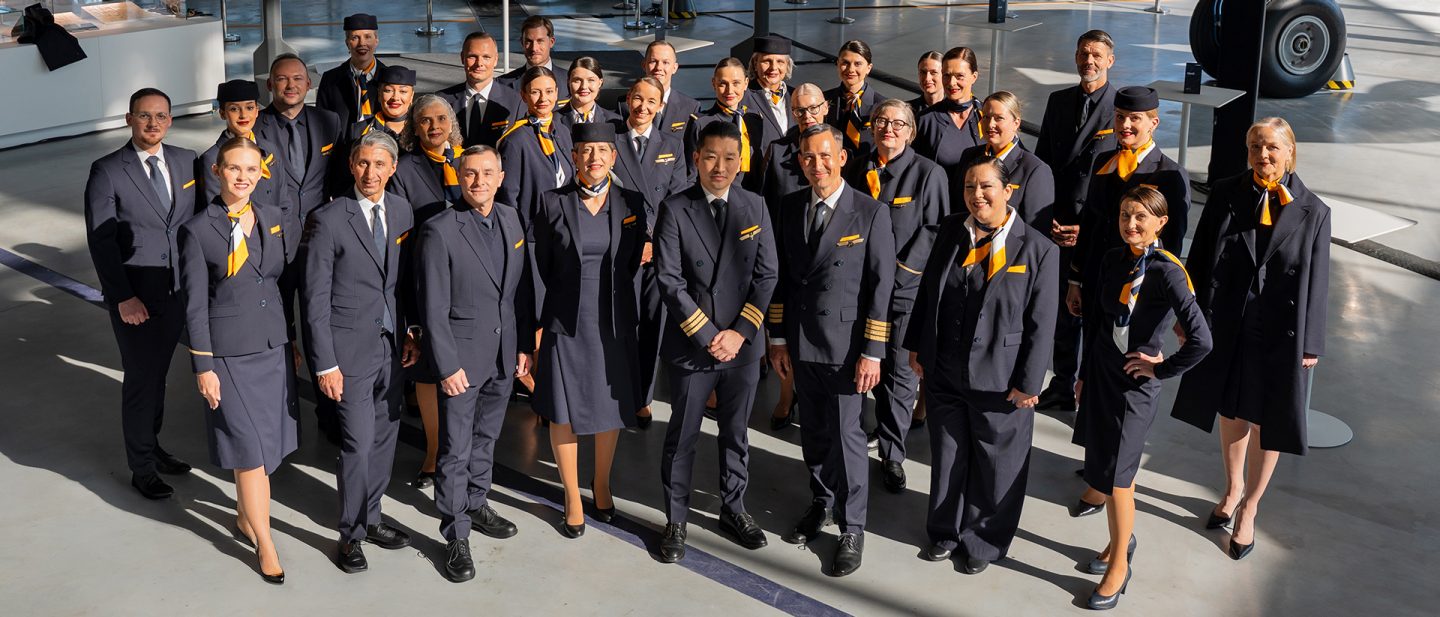 Group photo of airline crew in uniform in a bright airport hall, including pilots and cabin crew.