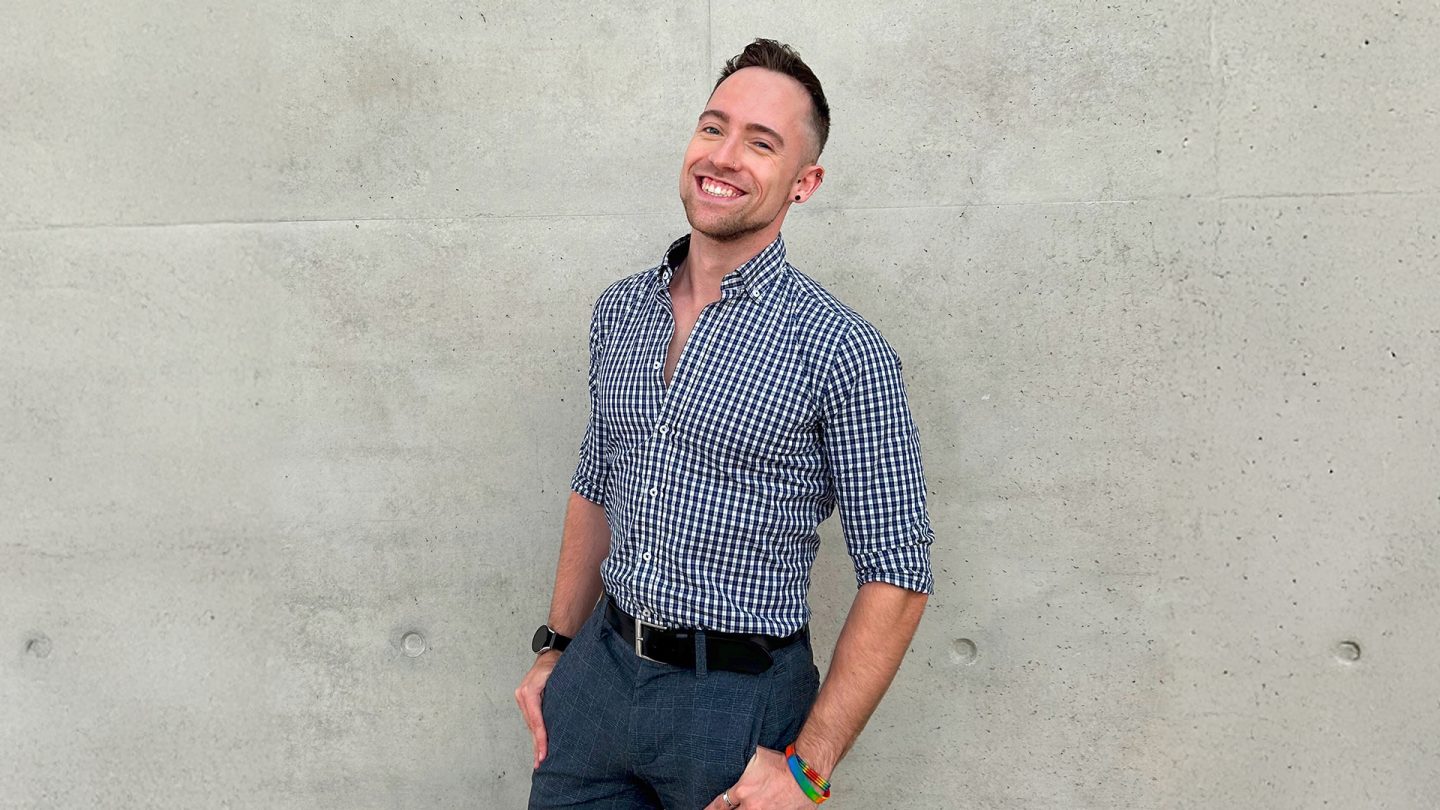Smiling man with bracelets in rainbow colors in front of a concrete wall
