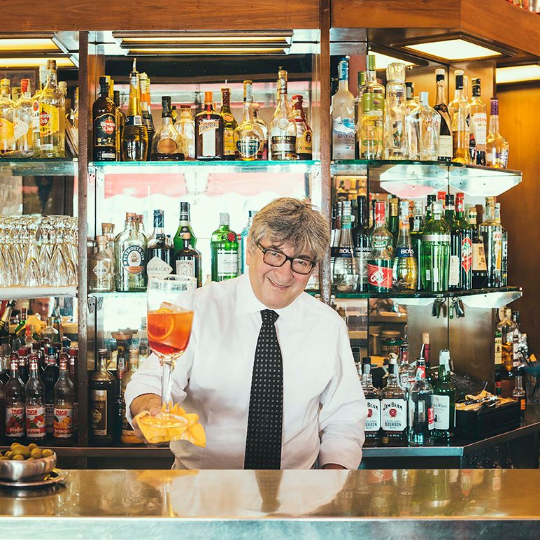 Friendly bartender serving a drink in a well-stocked Bar Basso in Milan