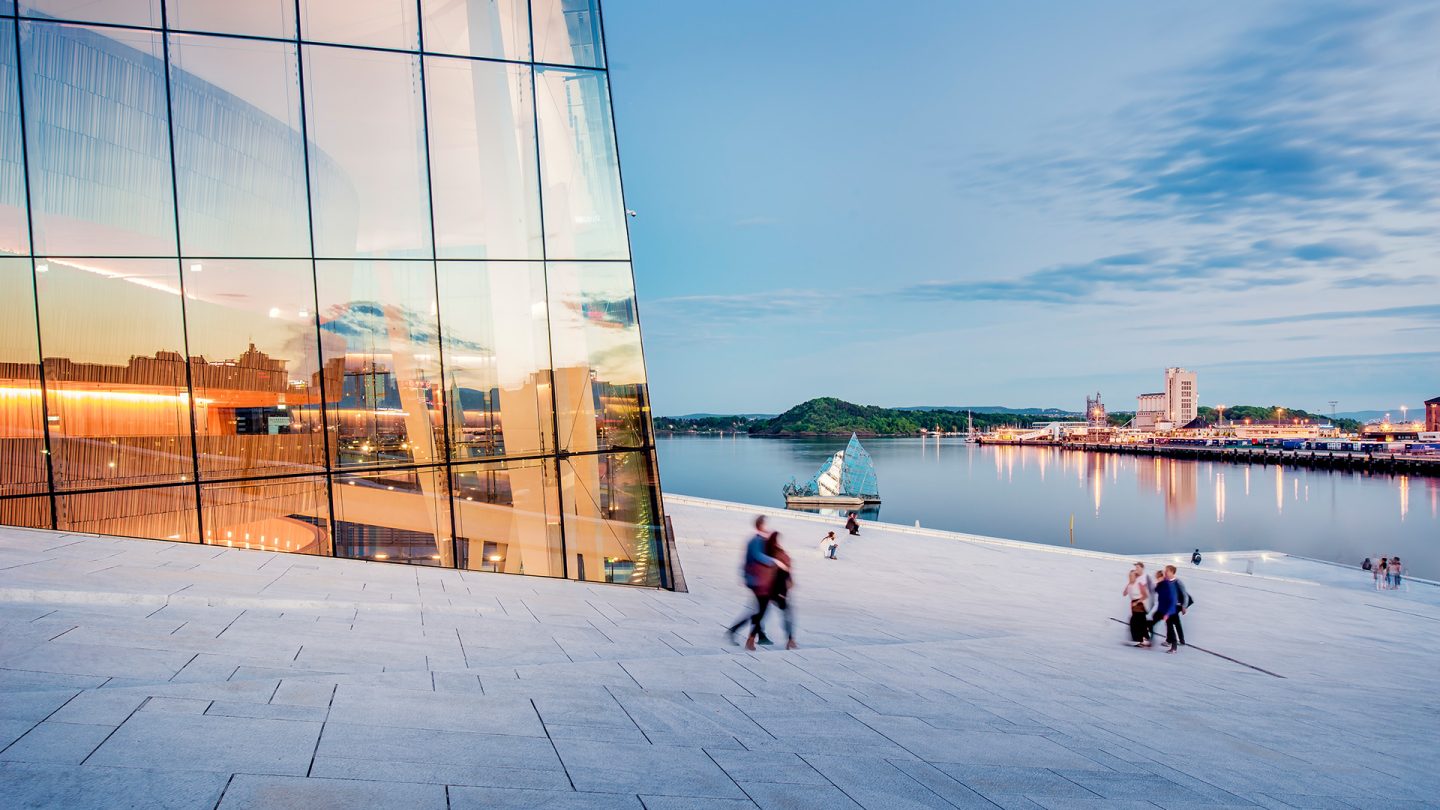 The glass facade and walkable roof of the Oslo Opera House meet the Oslofjord at dusk