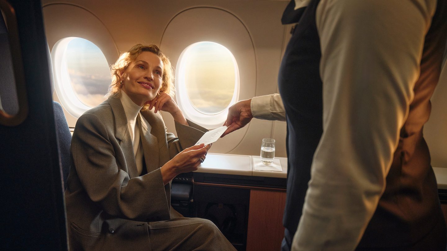 Flight attendant hands a card to a first class passenger.