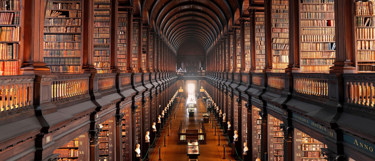 Majestic library interior in Dublin with tall arched ceiling, rows of wooden bookshelves filled with books, and long central aisle