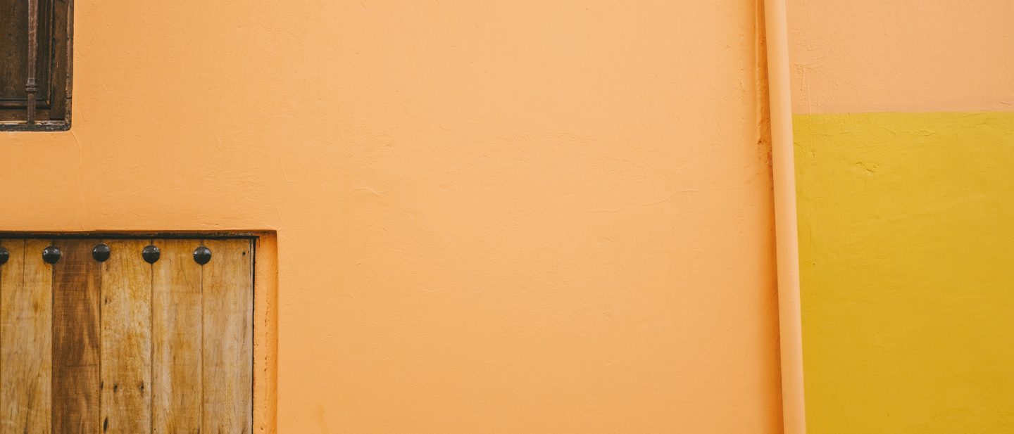 Close-up of a wall featuring orange stucco and a yellow stripe