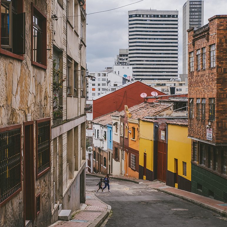 Steep street with colorful houses and modern skyline in the background in Bogotá